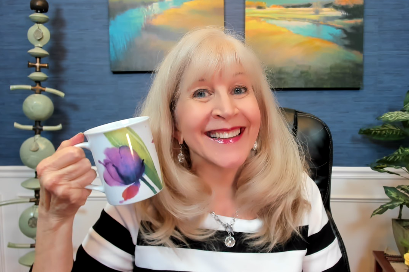 Smiling blonde woman holding a mug with a purple tulip.